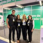 Estande de tecnologia em feira da construção com construtores analisando gestão de pós-obra em tela grande
